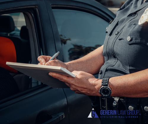 A person in a dark uniform writes notes on a clipboard beside an open car window, with an orange seat visible inside the vehicle.